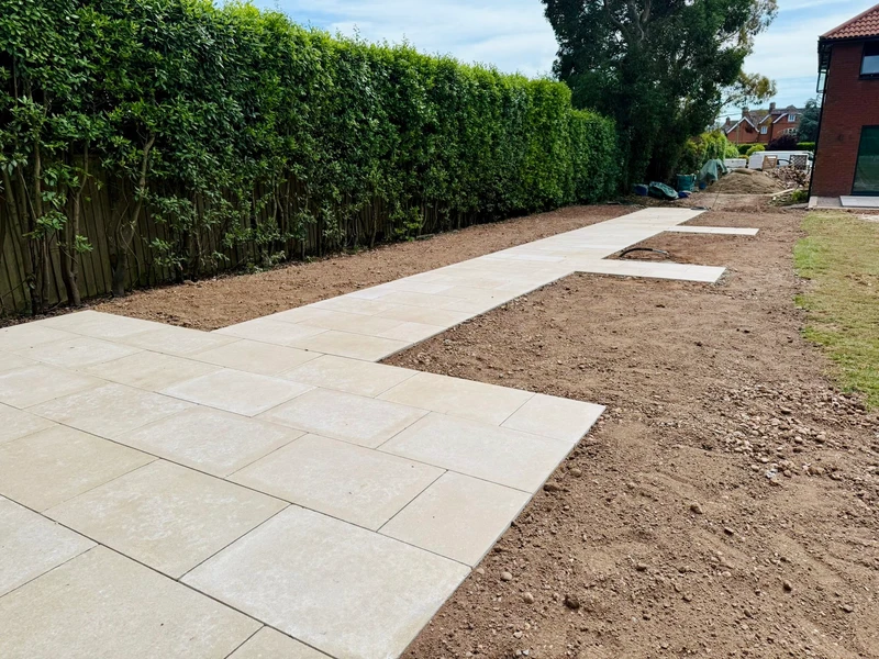 A new stone path and patio taking shape at the rear of a house, with the beds either side still to be finished