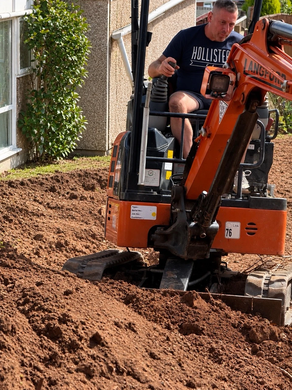 Graham at work on a mini digger, levelling ground beside a house