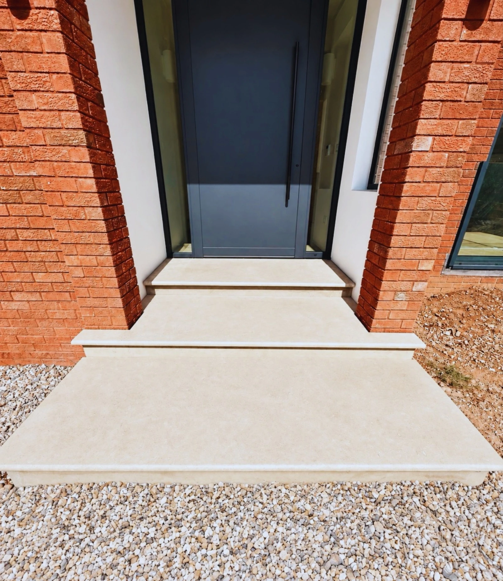 Pale stone steps up to a front door, edged in brick with a pebble border either side