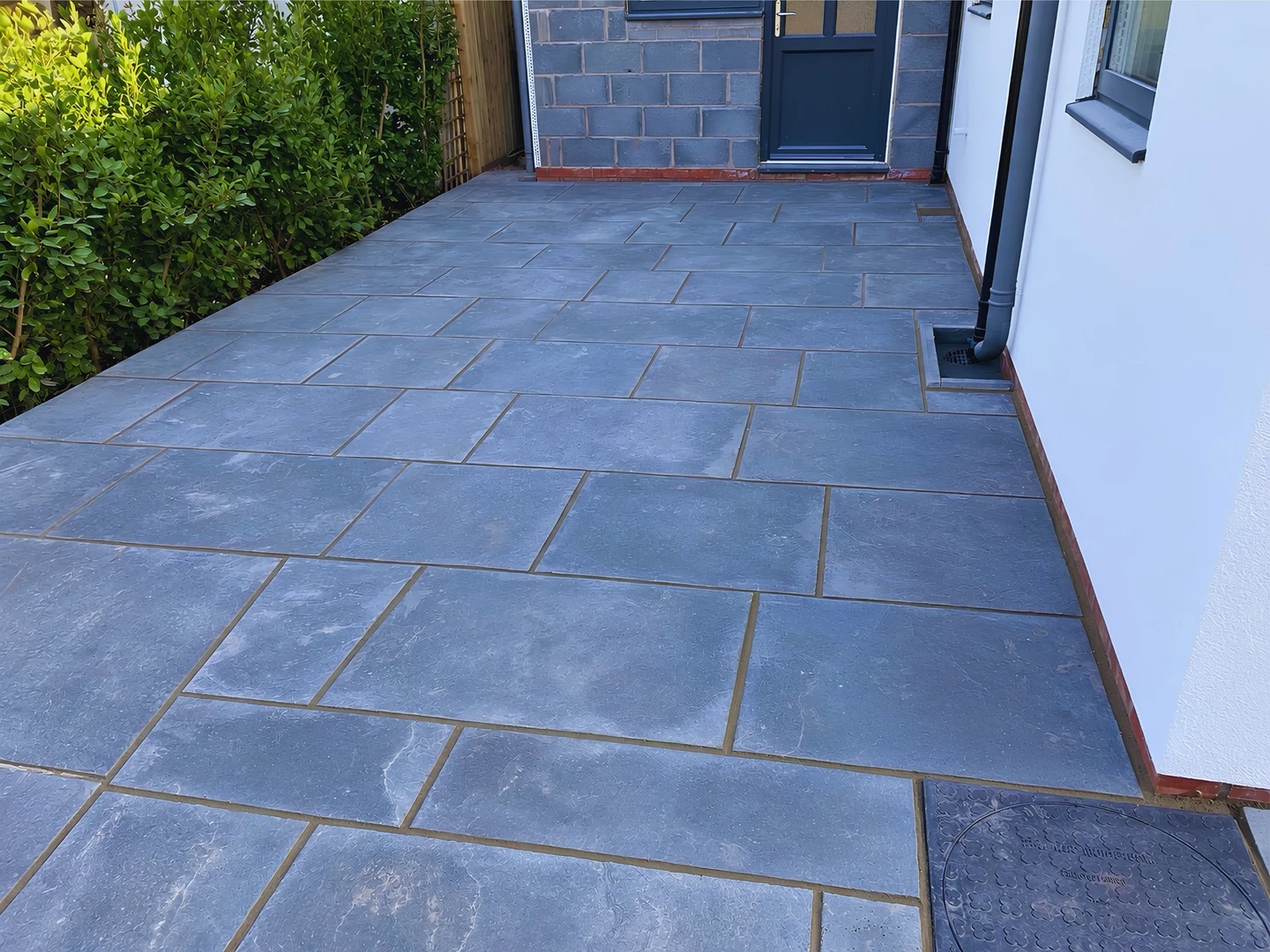 A newly laid dark stone-effect patio running the width of a house, up to the back door